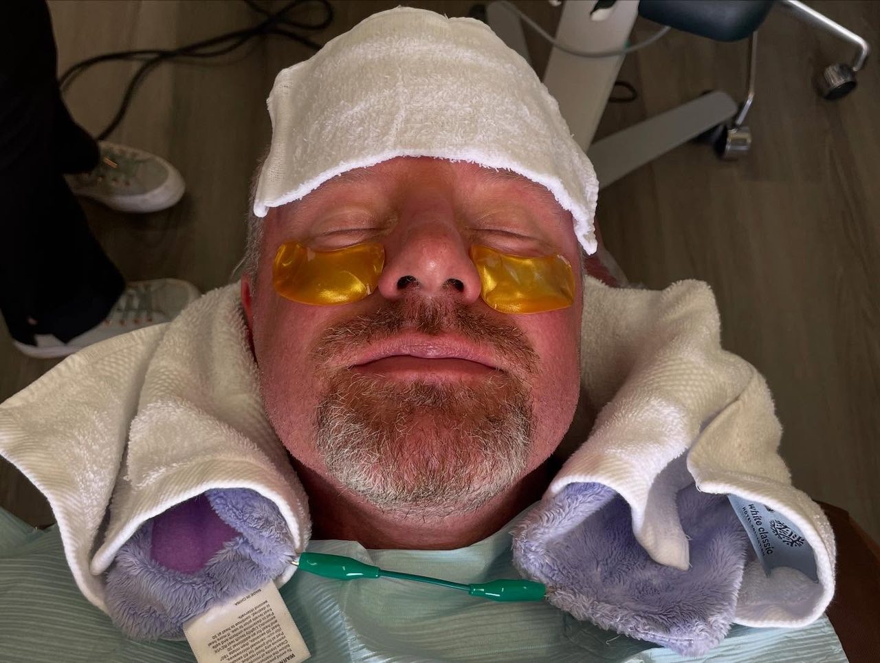 Relaxed Old Betsy Dental patient with an eye mask, a warm towel on the forehead, and a plush towel around the neck — comfort amenities for nervous patients